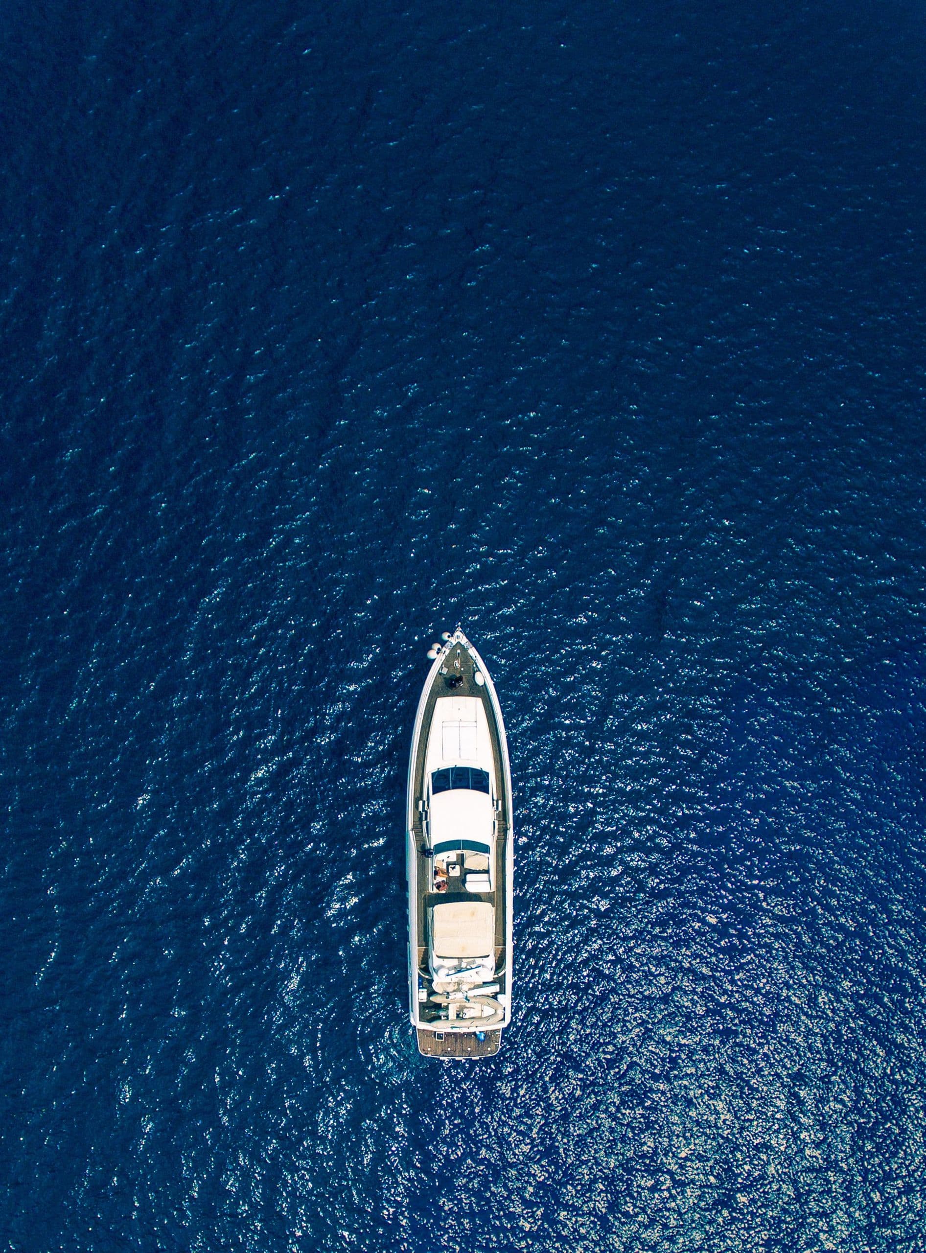 Белая моторная яхта в открытом море, вид сверху на глубокую синюю воду