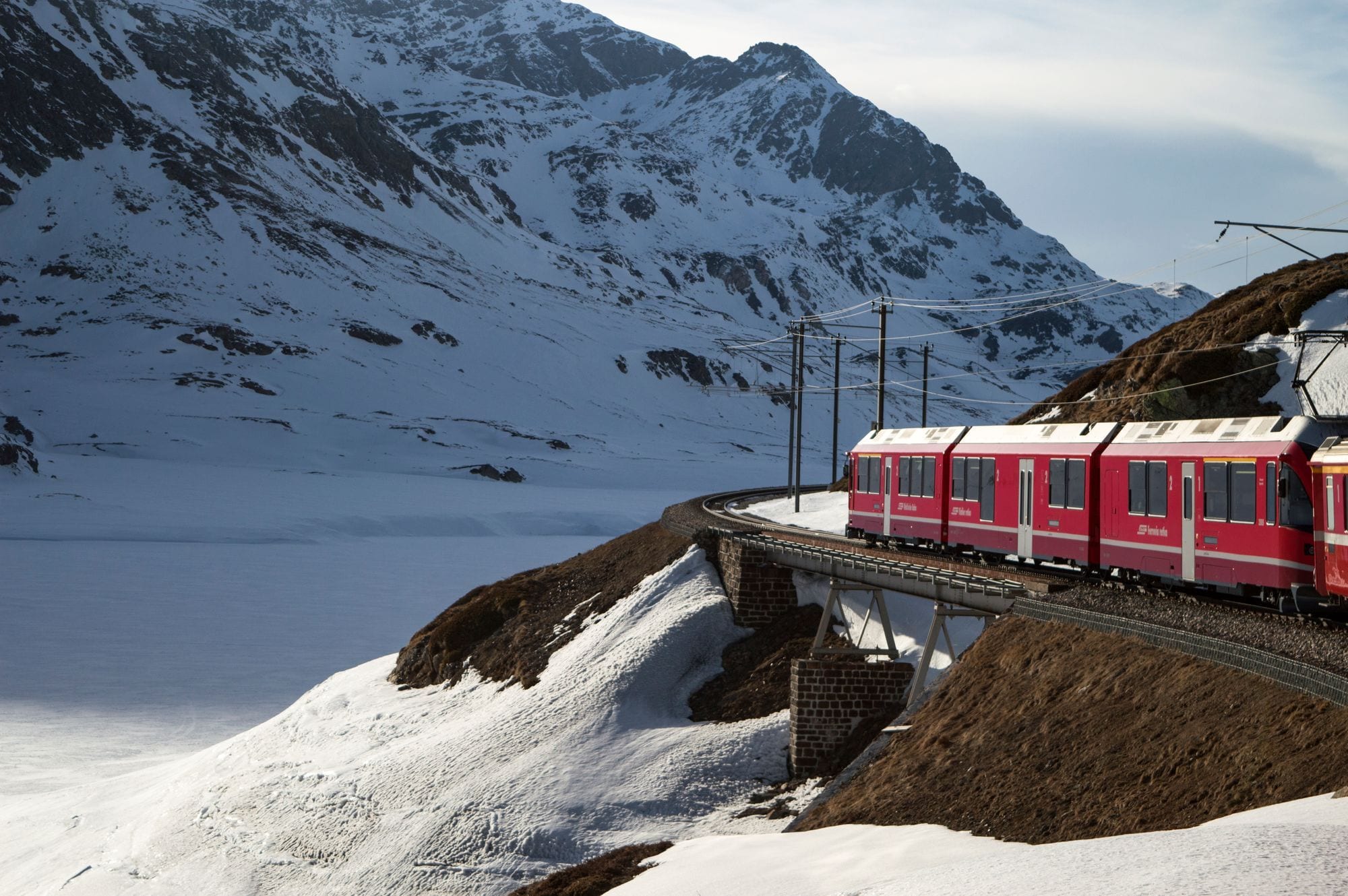 Красный поезд Bernina Express на мосту среди заснеженных гор, Швейцарские Альпы